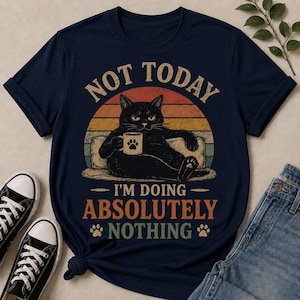 May include: A navy blue t-shirt featuring a graphic of a black cat holding a mug, set against a retro sunset background. The text reads NOT TODAY I'M DOING ABSOLUTELY NOTHING, accompanied by two small paw print icons in a distressed, vintage-style font.