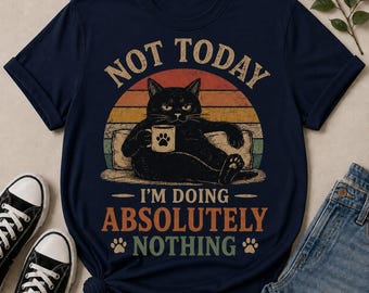 May include: A navy blue t-shirt featuring a graphic of a black cat holding a mug, set against a retro sunset background. The text reads NOT TODAY I'M DOING ABSOLUTELY NOTHING, accompanied by two small paw print icons in a distressed, vintage-style font.