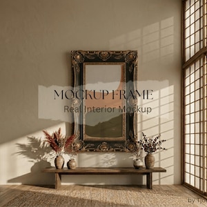 May include: An ornate, dark-framed mockup frame hangs on a neutral wall. The frame is above a wooden bench with vases and dried floral arrangements. The text "MOCKUP FRAME Real Interior Mockup" is visible on the image.