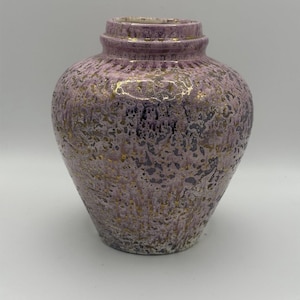 Puede incluir: Un jarrón decorativo de cerámica con un cuerpo bulboso y un cuello estrecho. El jarrón es principalmente lavanda con detalles dorados y gris oscuro. La superficie tiene un aspecto texturizado y moteado. El jarrón es adecuado para la decoración del hogar.