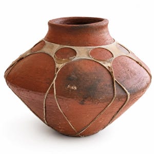 May include: A terracotta-colored clay vessel with a wide, angular midsection and a narrow neck. The exterior is decorated with a light-colored, thin, web-like lattice pattern that wraps around the upper body, creating circular shapes.