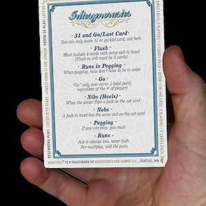 以下が含まれることがあります： カードゲーム「Idiosyncrasies」のルールが書かれたカード。白い背景に青い装飾とテキストが施されています。カードは人の手で持たれています。