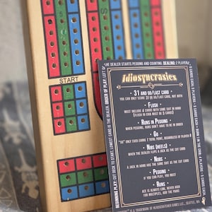 以下が含まれることがあります： 赤、緑、青のトラックが付いた木製のクリベッジボードと、「Idiosyncrasies」という単語とゲームルールが書かれた黒いカード。 ボードには「スタート」セクションとペグ用の穴があります。