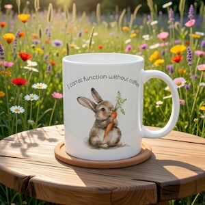 May include: White ceramic mug featuring a bunny illustration holding a carrot, with the text "I carrot function without coffee." The mug rests on a cork coaster. The background shows a vibrant field of flowers, set on a wooden table.