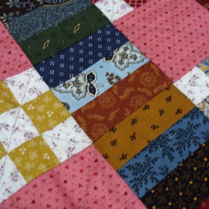 May include: A patchwork quilt with a variety of colorful fabrics and patterns. The quilt is made up of squares and triangles, and the colors include pink, blue, brown, yellow, and white.