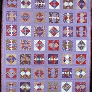 May include: A rectangular quilt featuring a grid of thirty-six square blocks set against a light purple background. Each block contains a smaller diamond-shaped pattern made of various multi-colored fabric squares in shades of red, purple, and white.