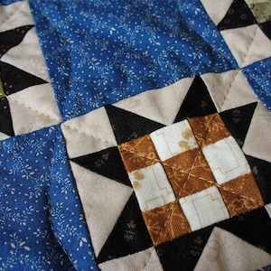 May include: A quilt made of fabric squares in shades of blue, black, white, and brown. The squares are sewn together in a pattern of stars and squares.