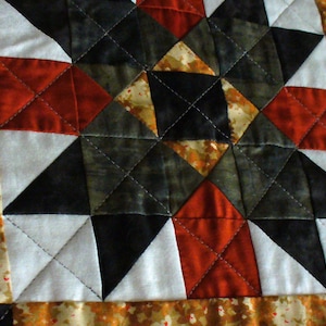 May include: A quilt block with a star pattern in shades of black, white, red, and brown. The block is made up of triangles and squares.