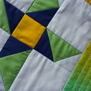May include: A close-up of a quilt with a star pattern in shades of green, blue, and yellow. The quilt is made of squares and triangles, and the fabric is textured.