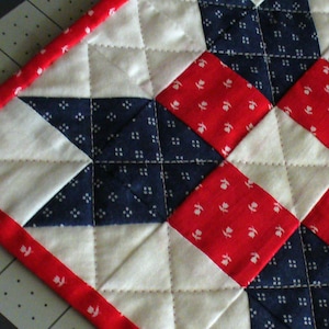 May include: A red, white, and blue quilted fabric with a diamond pattern. The fabric is made of cotton and has a soft, textured feel.