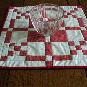 May include: A red and white quilted table runner with a clear glass bowl in the center.