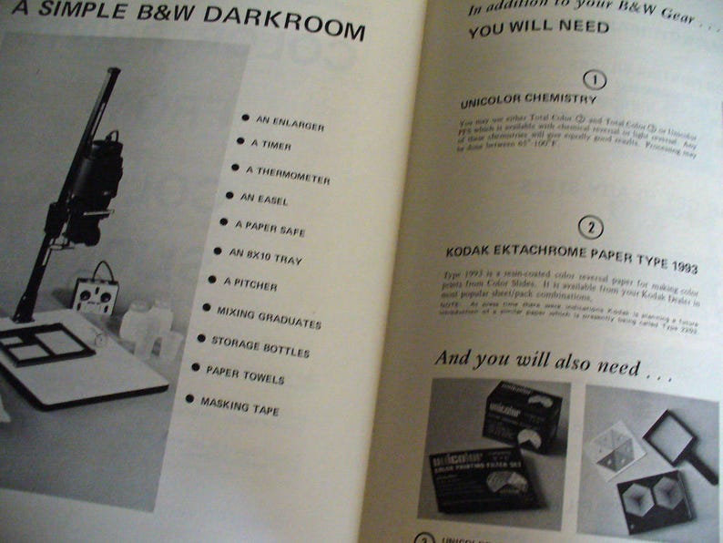 May include: An open instructional book page titled A SIMPLE B&W DARKROOM featuring a black and white photograph of a photographic enlarger and a list of equipment including a timer, thermometer, easel, paper safe, tray, pitcher, and bottles.