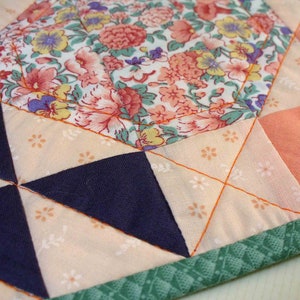 May include: A close-up of a quilt with a floral pattern in the center and a geometric pattern in the surrounding sections. The quilt is made of different fabrics in shades of pink, orange, blue, and green.