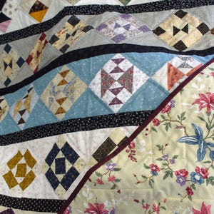 May include: A handmade quilt with a patchwork design. The quilt features various geometric patterns in shades of blue, yellow, white, and black. The border is a floral pattern with red, pink, and blue flowers. The quilt is a traditional craft item.