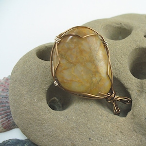 May include: A gold-toned wire wrapped around a light brown, irregularly shaped stone pendant. The pendant has a wire loop for hanging.