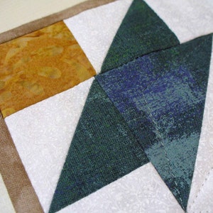 May include: A close-up of a patchwork quilt with a brown border. The quilt is made of white, green, and orange fabric. The fabric has a textured, woven look.