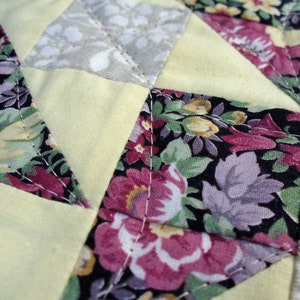 May include: A close-up of a quilt made with various fabrics. The quilt is made with a patchwork of different floral patterns in shades of pink, purple, and green. The quilt is sewn together with white thread.