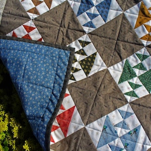 May include: A quilt with a patchwork design featuring various geometric shapes and patterns in shades of blue, green, red, white, and brown. The quilt is made with a variety of fabrics, including floral prints and solid colors.