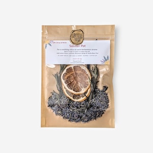Può includere: Un sacchetto di carta marrone contenente un kit per pentola a fuoco lento. Il kit include fette di limone essiccate, lavanda e rametti di rosmarino. L'etichetta recita "Simmer Pot" e fornisce istruzioni per l'uso. Il sacchetto è sigillato con un timbro di cera.