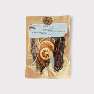 May include: A clear plastic bag filled with dried orange slices, cinnamon sticks, rosemary sprigs, and other spices. The bag has a label that reads "Summer Pot" and "Orange Spice". A gold seal with a leaf design is at the top.