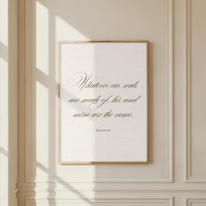 May include: A framed print featuring the quote "Whatever our souls are made of, his and mine are the same." by Emily Brontë. The text is in a flowing script on a cream backdrop, enclosed in a slender, light brown frame.
