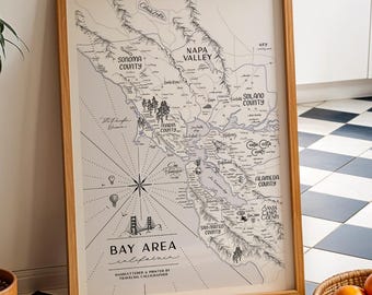 May include: A framed map print of the San Francisco Bay Area in California, featuring black line illustrations of regional landmarks, counties, and a compass rose on a cream background, with the text Bay Area California printed at the bottom.