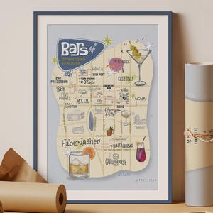 May include: A framed print titled "Bars of Downtown San Jose" with a map-like design featuring illustrations of cocktails and bar names. The print is in a blue frame, with a roll of paper and twine in the foreground.