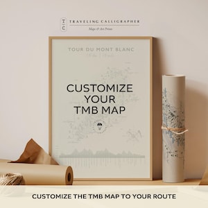 May include: A framed print of a Tour du Mont Blanc map with beige background and black text reading CUSTOMIZE YOUR TMB MAP, alongside a rolled paper map tied with twine. The print features topographical lines, a compass, and elevation data.