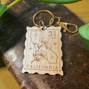 May include: Wooden keychain with a gold metal ring and clasp. The keychain features a stylised outline of the state of California with a poppy flower and the text "31" and "CALIFORNIA".