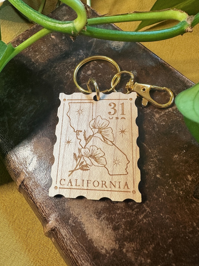 May include: Wooden keychain with a gold metal ring and clasp. The keychain features a stylised outline of the state of California with a poppy flower and the text "31" and "CALIFORNIA".