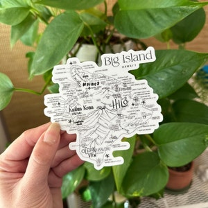 May include: A black and white sticker map of the Big Island of Hawaii. The map shows the major towns and cities, including Hilo, Kailua Kona, Waimea, and Pahoa. The map also shows the location of Volcanoes National Park and the Mauna Kea Observatories.