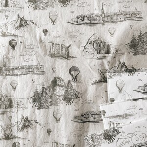 May include: A white background with a repeating pattern of black and white illustrations of hot air balloons, mountains, and buildings. The pattern is reminiscent of a vintage travel poster.