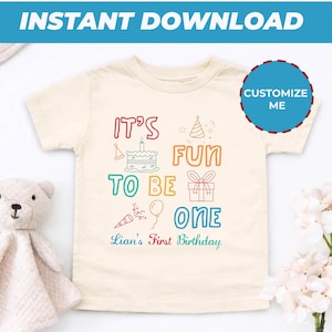 May include: Cream-coloured toddler t-shirt with the text "IT'S FUN TO BE ONE" in colourful letters and graphics. Includes a birthday cake, party hat, gift, and confetti. The text "Lian's First Birthday" is written below. A blue circle with "Customize Me" is on the right.