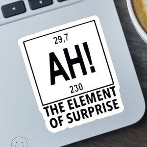 May include: A square white sticker with a black border featuring the text AH! in large letters, the number 29.7 at the top, the number 230 at the bottom, and the text THE ELEMENT OF SURPRISE printed below the square frame.
