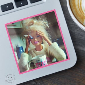 May include: A square sticker featuring a blonde doll with messy hair wearing a cream-colored sweater. The doll holds a lit cigarette in one hand and rests the other on its forehead. A white mug with the pink text GTED is held in front of the doll.