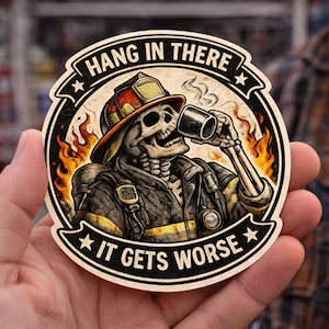 May include: A circular sticker featuring a skeleton dressed in a firefighter uniform and helmet, drinking from a mug amidst flames. The text HANG IN THERE is arched at the top, and IT GETS WORSE is arched at the bottom in black lettering.