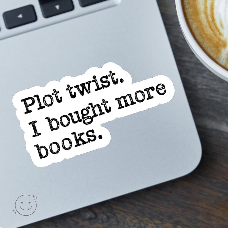 May include: A white sticker with the text "Plot twist. I bought more books." in black, placed on a laptop. A cup of coffee is visible in the background. The sticker has a rounded rectangle shape.