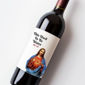 May include: A wine bottle with a label featuring an image of Jesus and the text "This Used To Be Water AD 33". The bottle is filled with red wine and has a dark burgundy neck.
