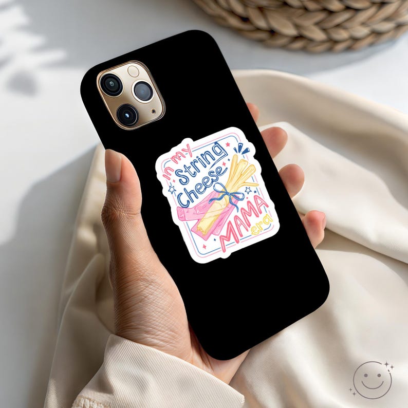 May include: Black iPhone case with a colourful sticker that says "My String Cheese Mama". The sticker features illustrations of string cheese and a bow. The phone case has a triple-lens camera.