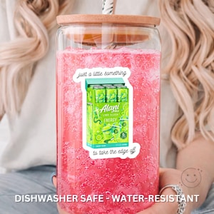 K&ouml;nnte beinhalten: Ein durchsichtiges Glas mit Bambusdeckel und Strohhalm, gef&uuml;llt mit einer leuchtend rosa Fl&uuml;ssigkeit. Ein Aufkleber auf der Vorderseite zeigt eine gr&uuml;ne Alani Nu Lime Slush Energy-Drink-Packung mit dem Text "just a little something" und "to take the edge off".