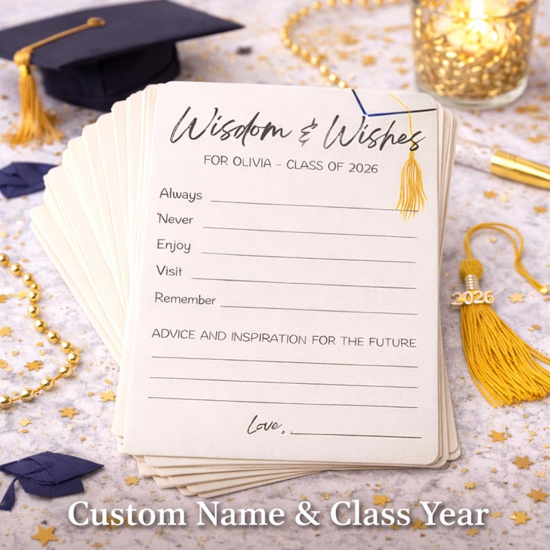 May include: A pile of ivory graduation advice cards, inscribed with "Wisdom & Wishes" and "FOR OLIVIA - CLASS OF 2026". The cards offer space for advice. A gold tassel and miniature graduation cap are also visible.