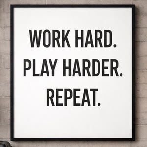 May include: A framed print with the text "WORK HARD. PLAY HARDER. REPEAT." in bold black letters on a white background. The frame is black, and the background is a brick wall.