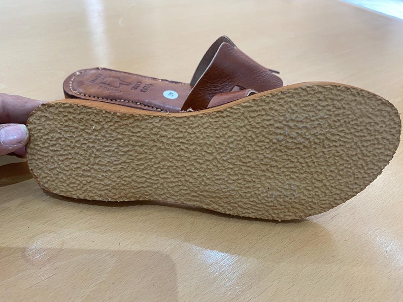 "A pair of artisan handcrafted Moroccan leather flat sandals featuring a classic -style strap. Made from high-quality natural grain leather with meticulous hand-stitching, shown from a top-down view on a neutral surface."