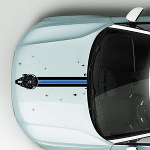 以下が含まれることがあります： SOLO FALCON VERSION BI-COLOR !というテキストが記されたステッカーが貼られた水色の車のボンネット。デザインには黒と青のストライプ、宇宙船のグラフィック、ボンネットの表面に散らばる小さな星の形が含まれています。