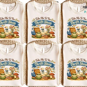 May include: Six white t-shirts with the text "Take Me To The Thrift Shop" in a blue banner. The design includes a duck, mushrooms, and other vintage elements. The shirts are arranged on a woven surface.