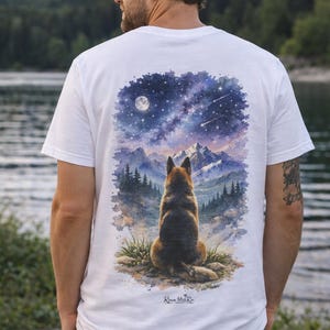 May include: White t-shirt with a watercolour illustration of a dog looking at a starry night sky above mountains. The design includes a full moon and shooting stars. The shirt has the text "Roam With Ro" at the bottom.
