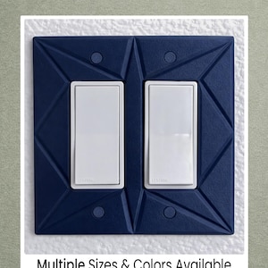 May include: A navy blue double light switch cover with a geometric design. The cover has two white rocker switches. The text "Multiple Sizes & Colors Available" is at the bottom of the image.