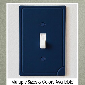 May include: A navy blue light switch cover with a white toggle switch. The cover has a rectangular shape with rounded corners and a raised border. The text "Multiple Sizes & Colors Available" is at the bottom.