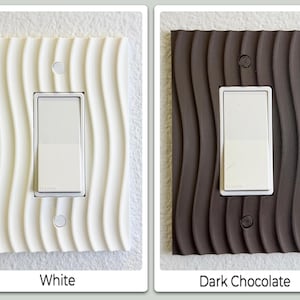 May include: Two light switch covers, one white and one dark chocolate, with a wavy, textured design. Each cover has a white switch and two small circular screw holes. The text "White" and "Dark Chocolate" are below the respective covers.