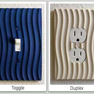 May include: Two electrical outlet covers. One is a dark blue toggle switch cover with a wavy pattern. The other is a cream-colored duplex outlet cover with a similar wavy design. The text below the blue cover says "Toggle", and the text below the cream cover says "Duplex".